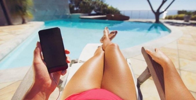 Woman-tanning-next-to a-crystal-clear-swimming-pool-holding-a-cellphone-wearing-a-red-bikini