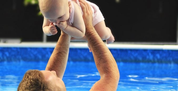 Father In Clear, Blue, Clean Swimming Pool Lifting His Baby Daughter The Air